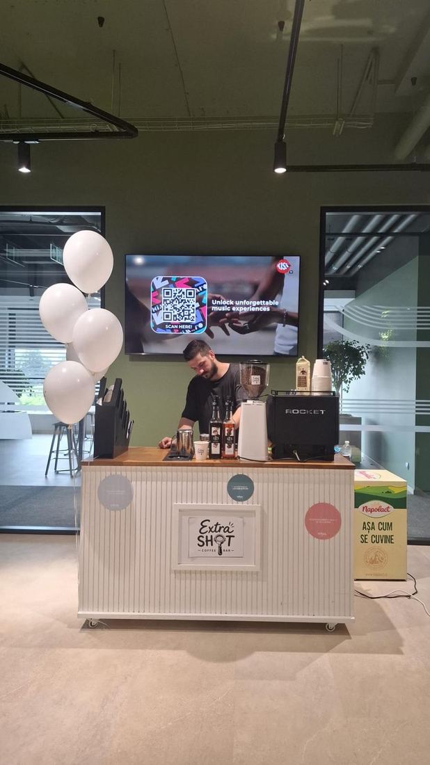 Barista ExtraShot pregătind cafea la un eveniment corporate, cu baloane și ecran de prezentare