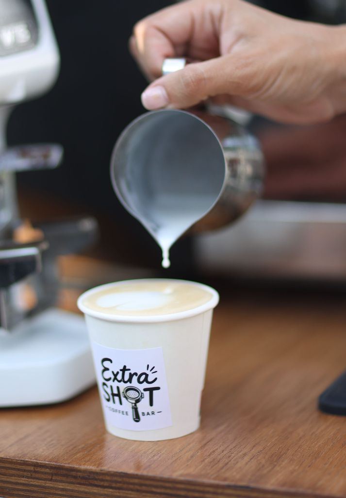 Barista ExtraShot turnând lapte pentru latte art într-o cană cu logo ExtraShot Coffee Bar